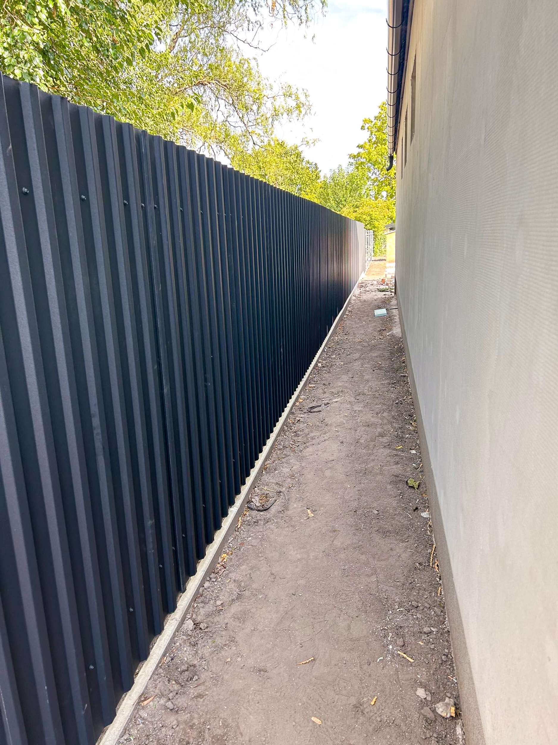 Antracit trapézlemez kerítés hosszú szakasza ház fal mellett