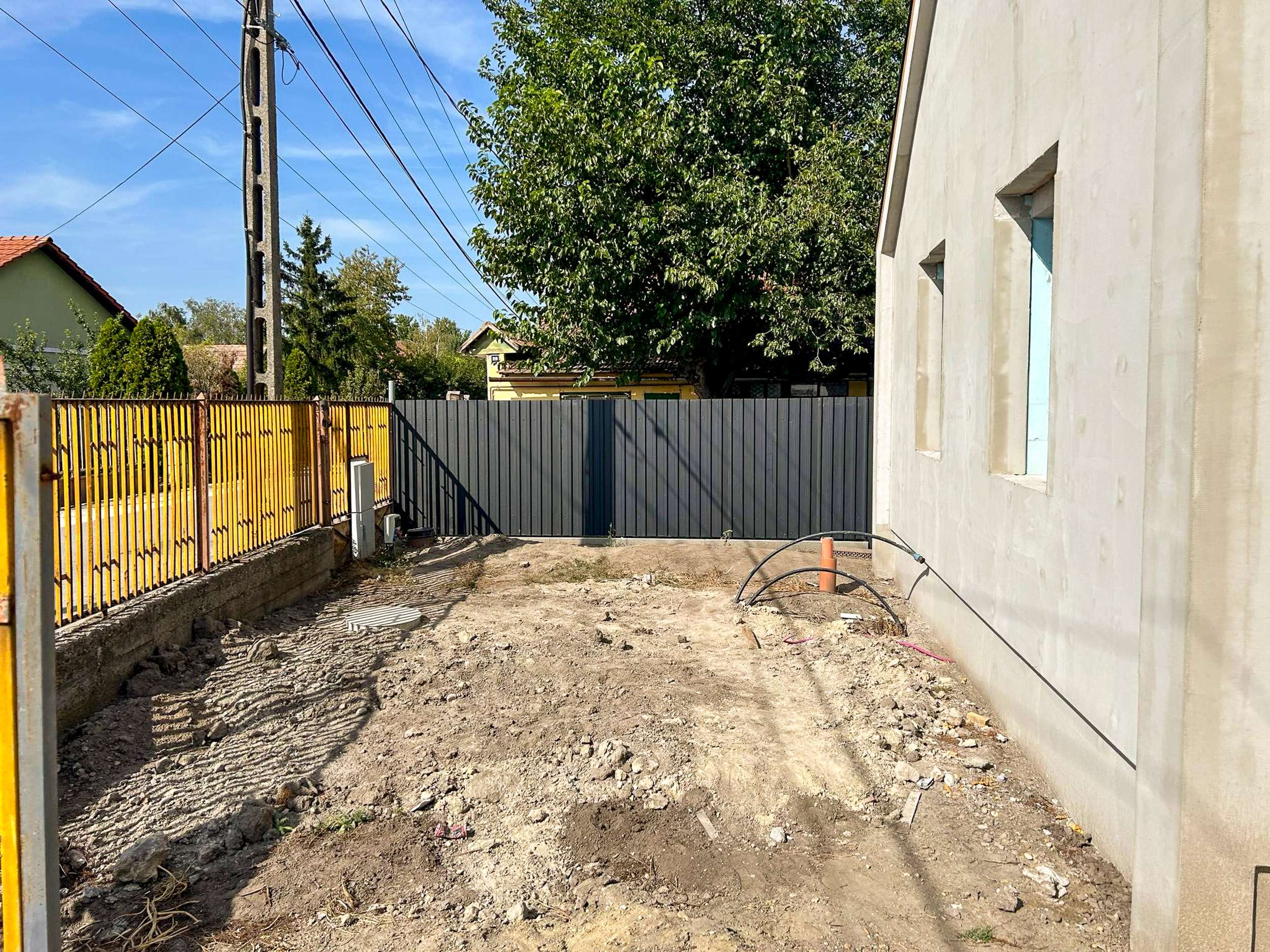 Szürke trapézlemez kerítés újépítésű ház mellett